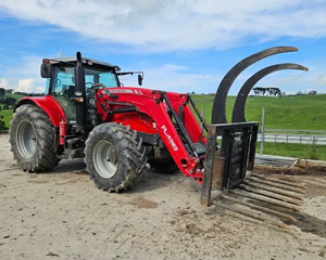 A bright red tractor with large muddy tires parked on a dirt path, set against a green rural landscape and blue sky.
