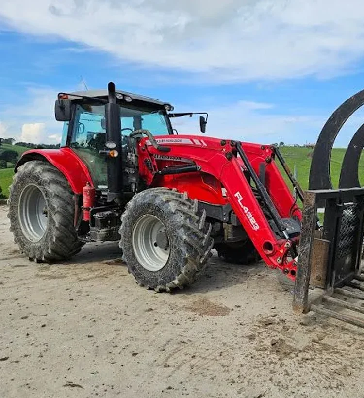 A bright red tractor with large muddy tires parked on a dirt path, set against a green rural landscape and blue sky.